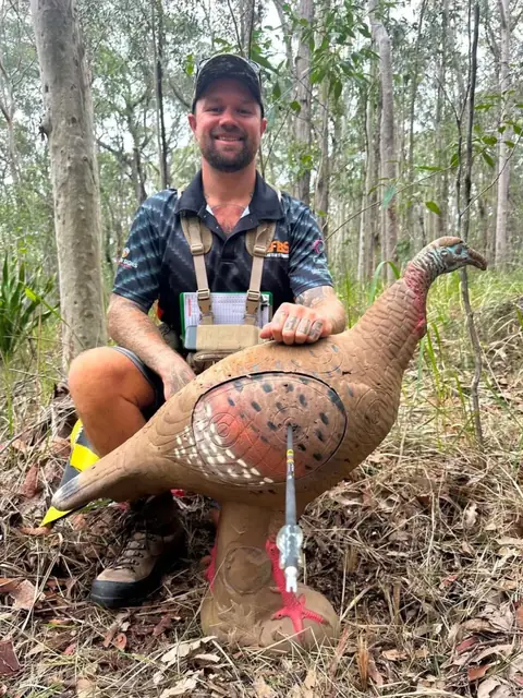 An archer behind a 3D turkey target with an arrow still in the foam.