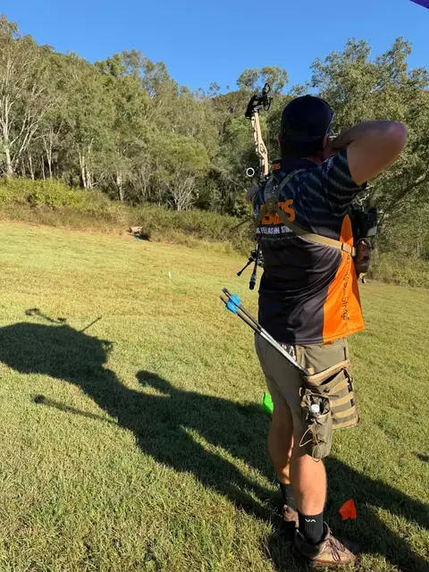 An archer seen from behind on the range with arrows in a hip quiver.