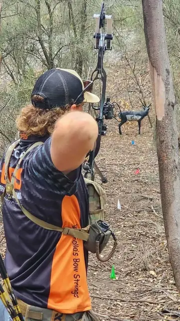 An archer steadying against a post on a bush course, drawing on a downhill target.