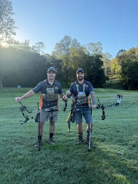 Two archers walking back across the grass with their bows after a round.