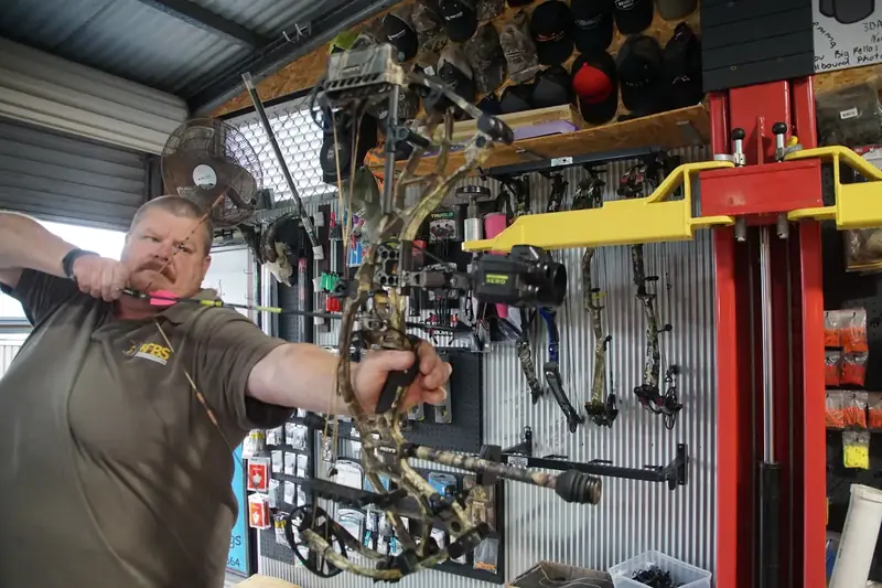 Tim at full draw in the workshop, with the bow wall behind him.