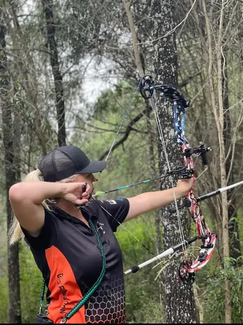 An archer at full draw among the gums with a camouflage compound bow.
