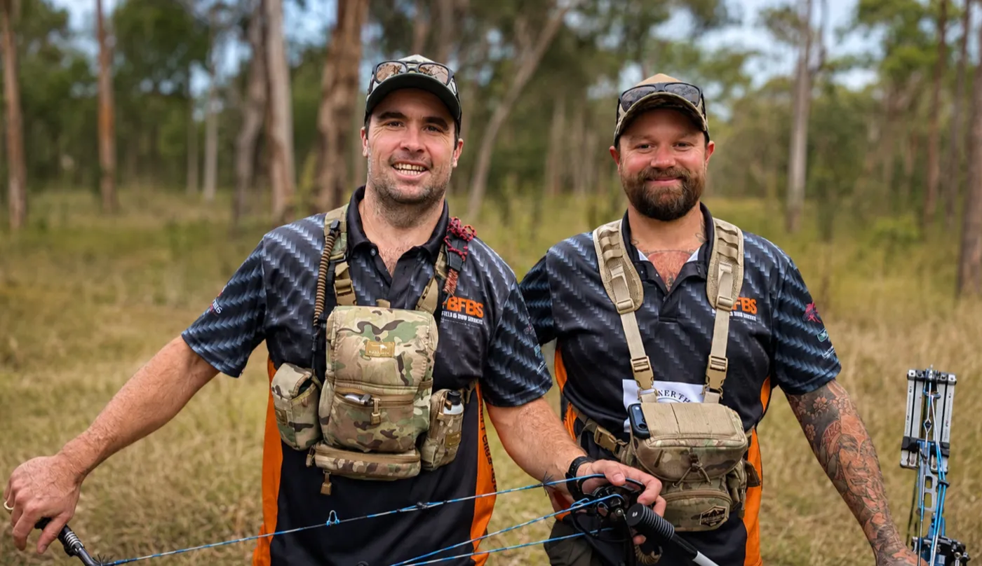 Two archers in Big Fella's team shirts on a field course, bows in hand.